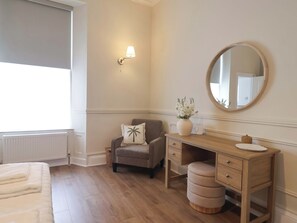 Ein Schlafzimmer mit Bett, Kommode, Stuhl, Lampe und Spiegel.