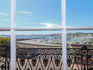 A marina with boats docked, a clear sky, and a view through a window with decorative iron railings. - Flat 2 The Moorings (Torquay)