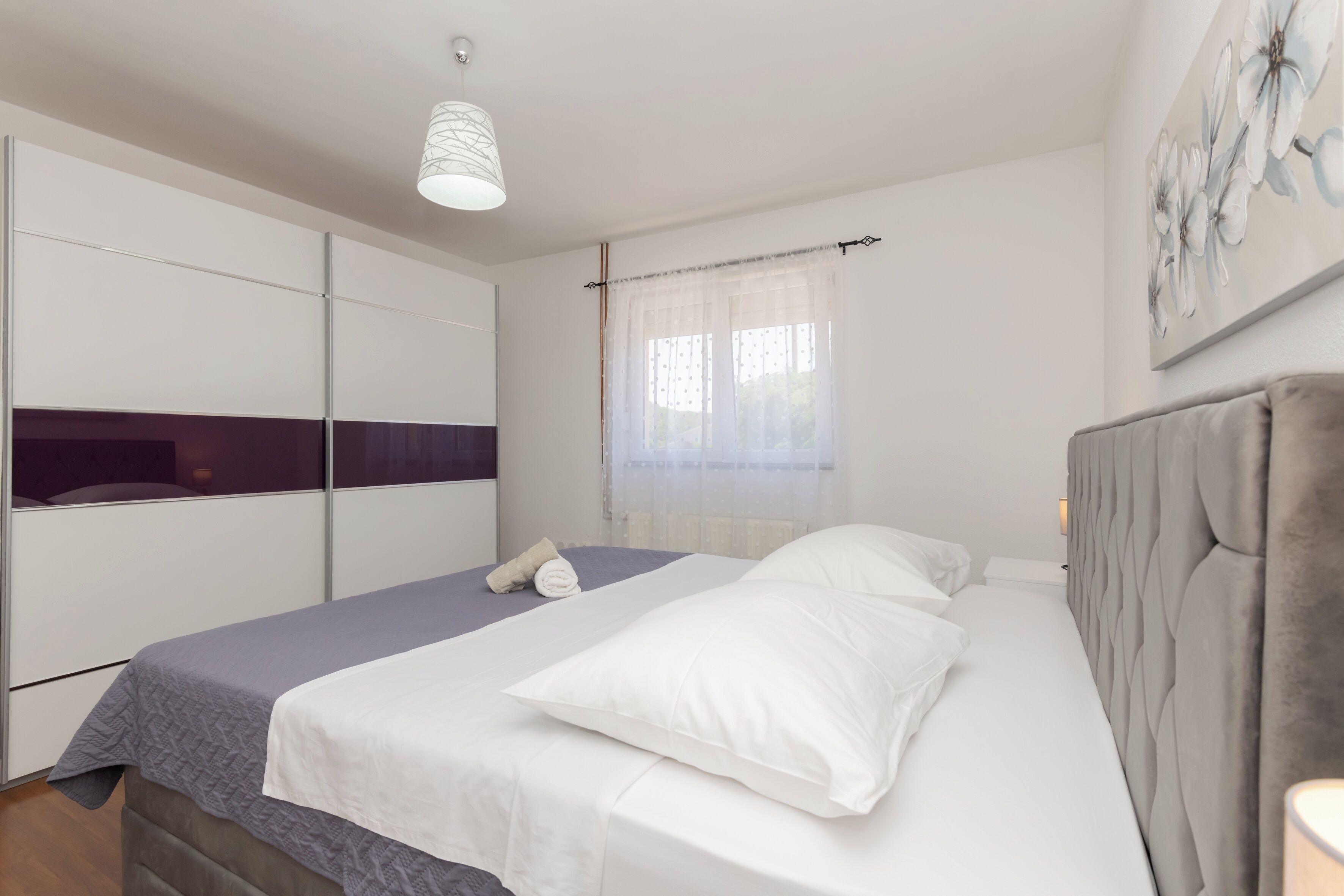 Un dormitorio con una cama, un armario, un ventanal con cortinas y una obra de arte en la pared.