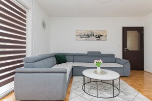 A modern living room with a grey sectional sofa, a round coffee table, and a cityscape painting on the wall.