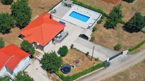 Vista aérea de uma propriedade residencial com piscina, casa com telhado vermelho, trampolim e entrada de veículos.