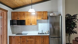 A kitchen with wooden cabinets, a stainless steel refrigerator, a microwave, and a pendant light.