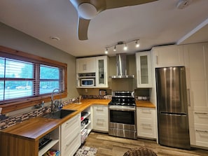 Una cocina moderna con armarios blancos, electrodomésticos de acero inoxidable, encimera de madera y una ventana con persianas.