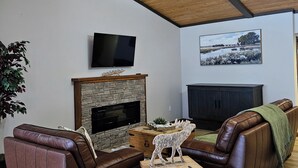 A living room with a stone fireplace, leather sofas, a television, and a wooden ceiling.