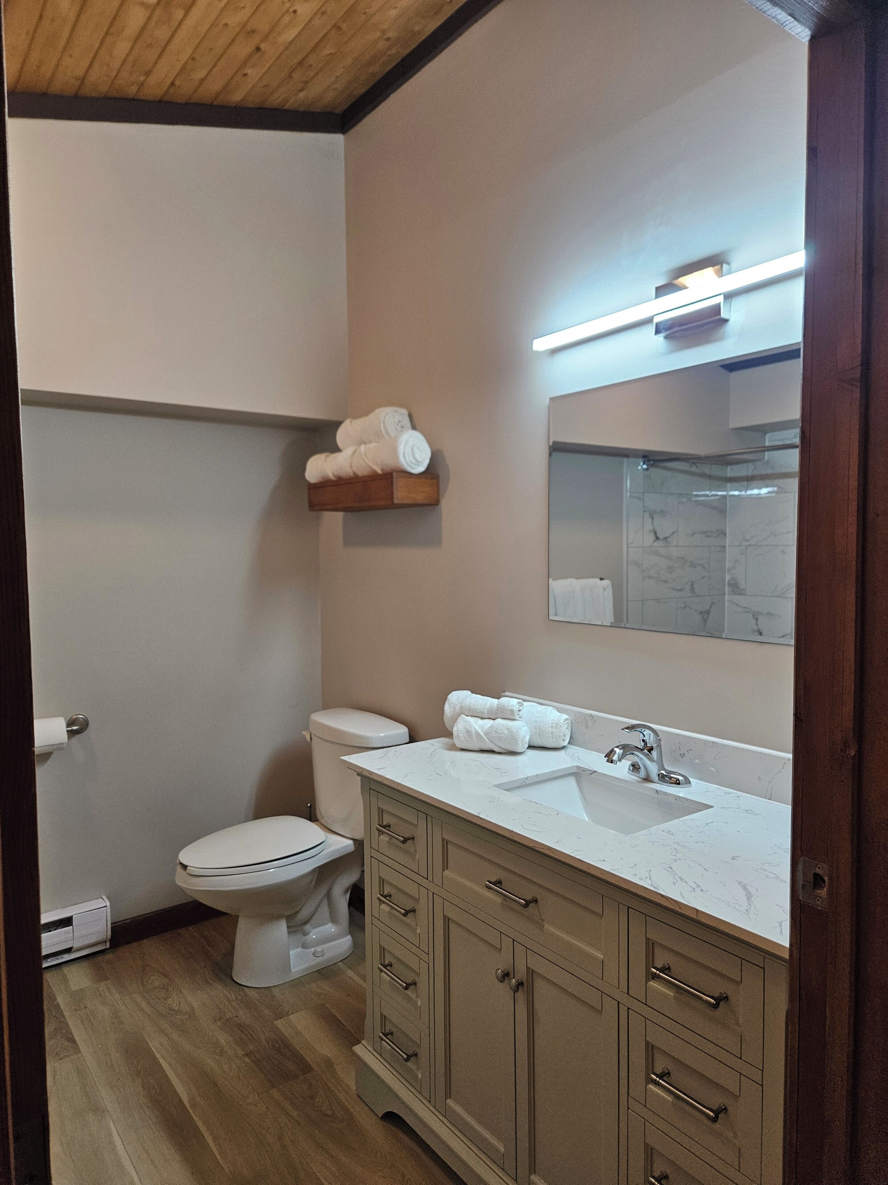 A bathroom with a toilet, sink, mirror, towel rack, and wooden floor.