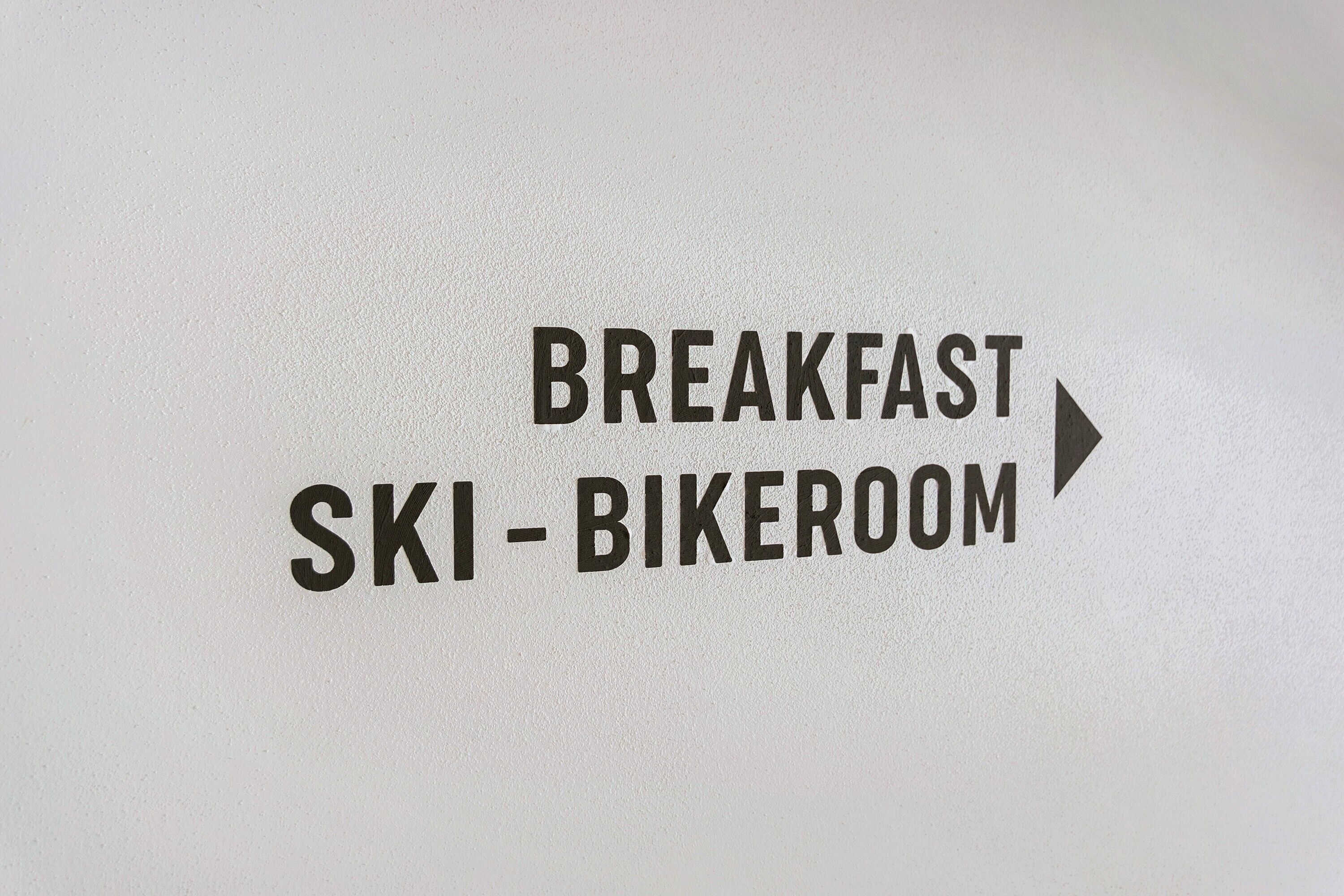 En skylt som visar vägen till skidförvaringen/rummet där man kan förvara skidor och cyklar inför frukosten.