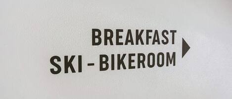 En skylt som visar vägen till skidförvaringen/rummet där man kan förvara skidor och cyklar inför frukosten.