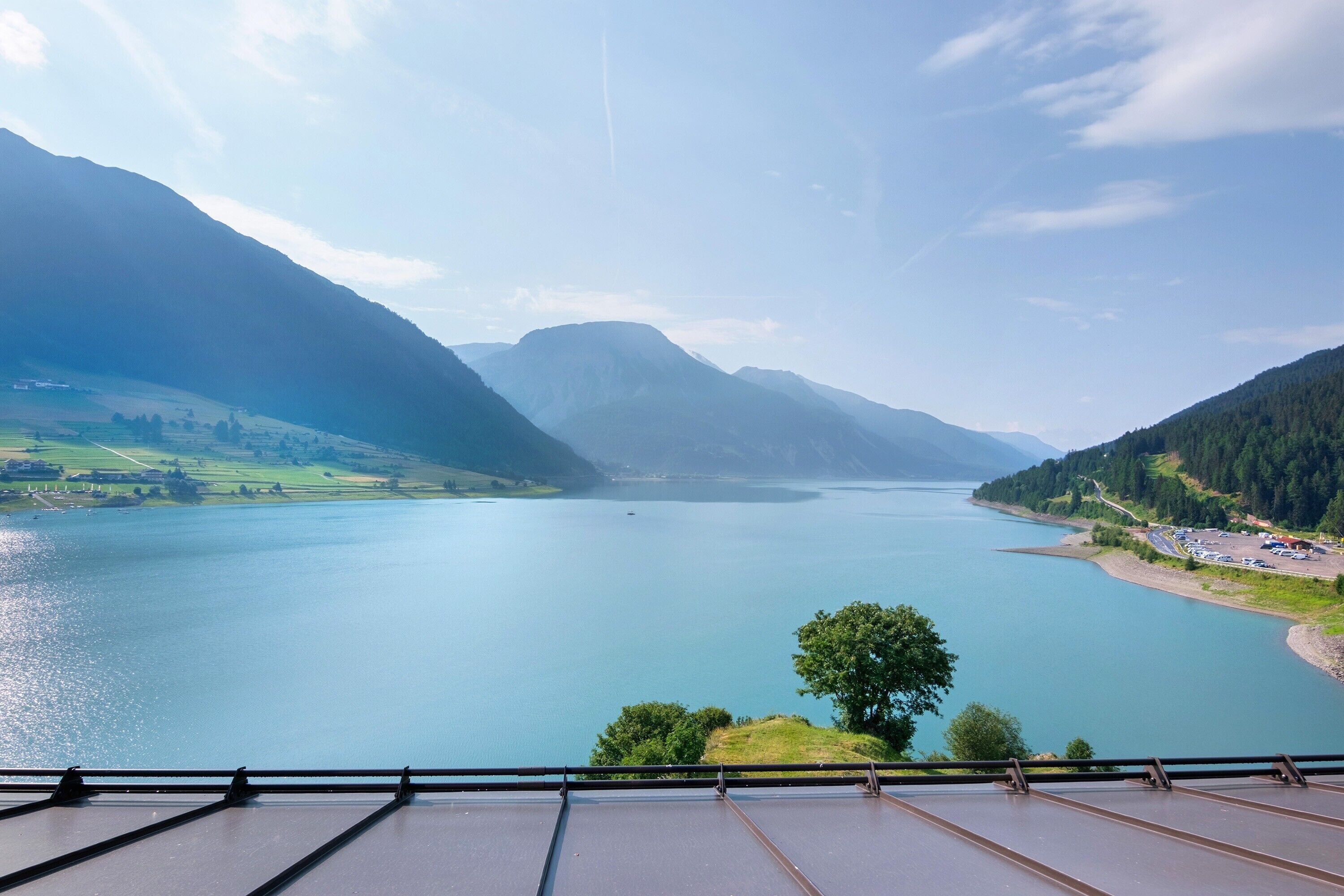 Una vista panoramica su un lago circondato da montagne, con cielo sereno e una costa lontana.