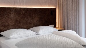 Un lit avec des oreillers blancs et une couverture à motifs, une table de chevet en bois et une tête de lit à motifs.