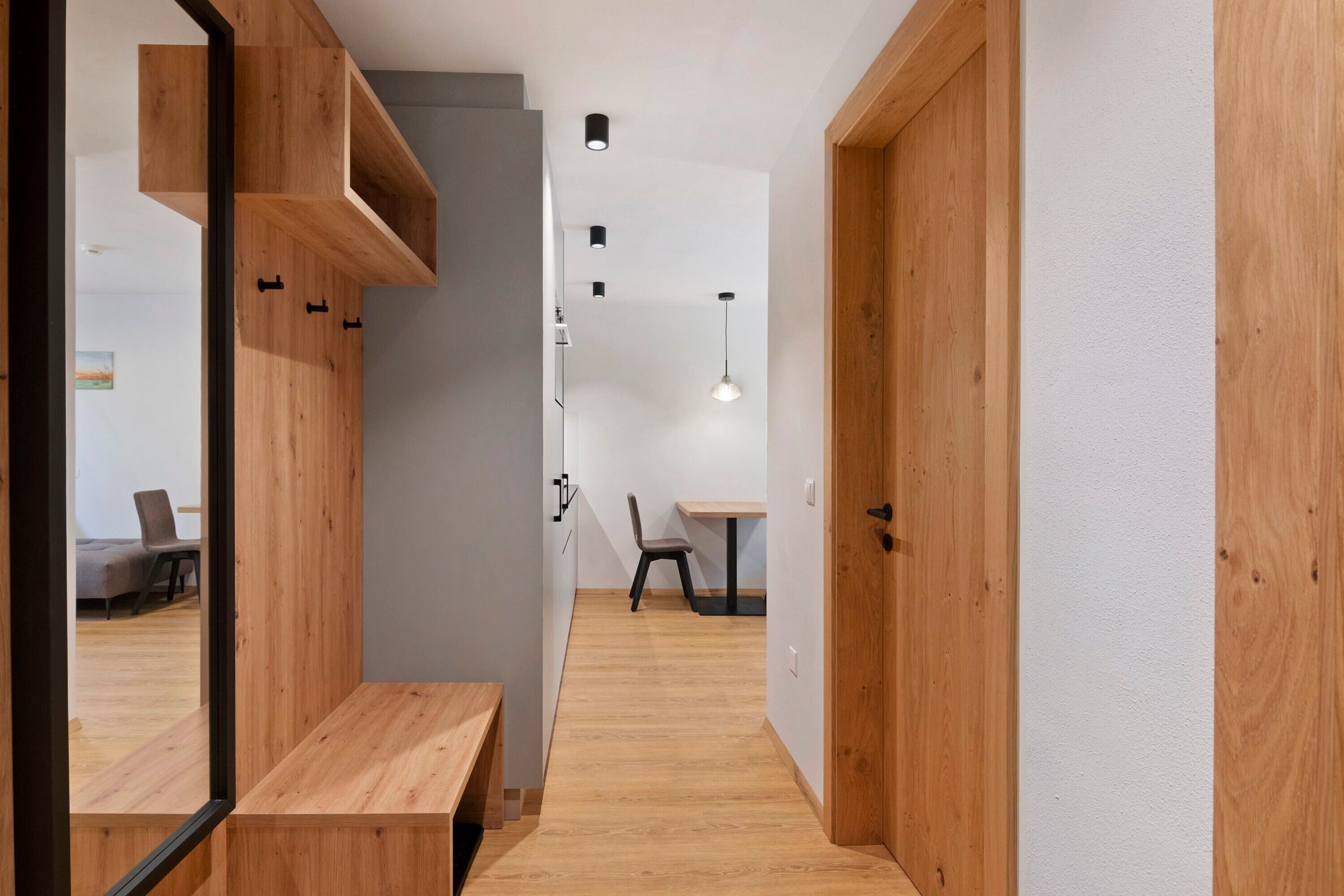 A hallway with wooden flooring, a bench, a table, and a chair.