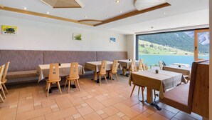 A restaurant with a view of a lake and mountains, featuring wooden furniture and a modern ceiling design.