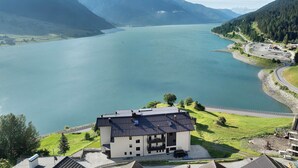 A lakeside hotel with a view of the lake and mountains, a parking area, and a building with a sloped roof. - Residence Froy Apartment 7 – Lake View, Whirlpool & Breakfast Included (Graun im Vinschgau)