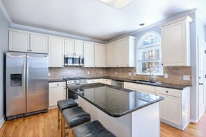 A modern kitchen with white cabinetry, a stainless steel refrigerator, a microwave, a stove, and a large island with bar stools. - Spacious 4BR Near Lassiter | Game Room & Basement (Marietta)