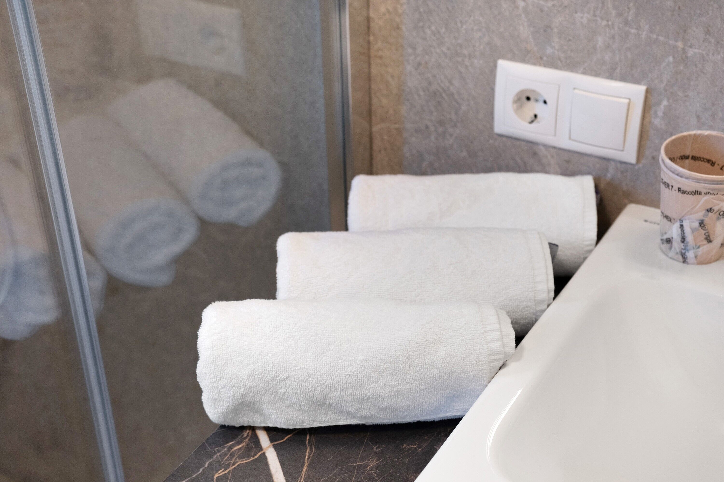 Un baño con mampara de vidrio, un lavamanos blanco y toallas ordenadas sobre el mostrador.