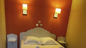 Una cama bien hecha con almohadas y toallas, un cabecero blanco, dos mesitas de noche con lámparas y un suelo de baldosas.
