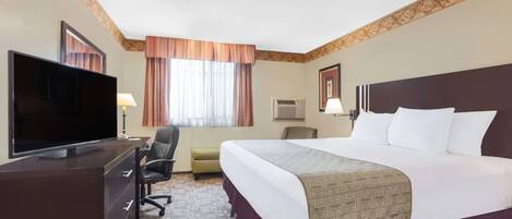 Habitación de hotel con cama, televisión, escritorio, silla y ventana con cortinas.