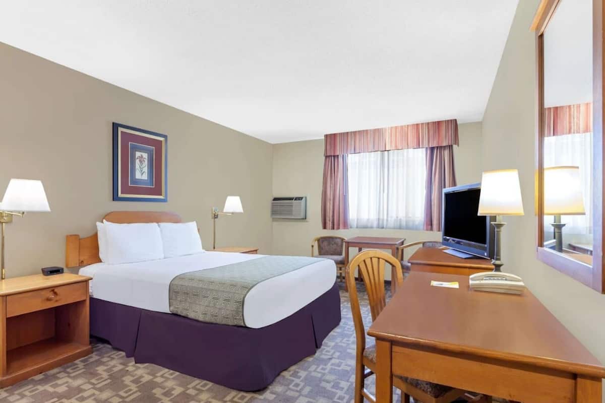 A hotel room with a bed, bedside tables, a desk with a chair, a television, and a window with curtains.