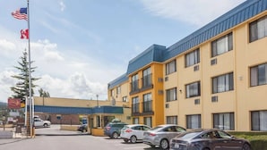 Ett hotell med flera våningar och ett blått tak, en parkeringsplats med flera bilar och en flaggstång med flaggor.