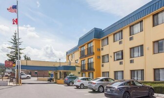 Un hotel de varios pisos con techo azul, un estacionamiento con varios coches y un asta con banderas.