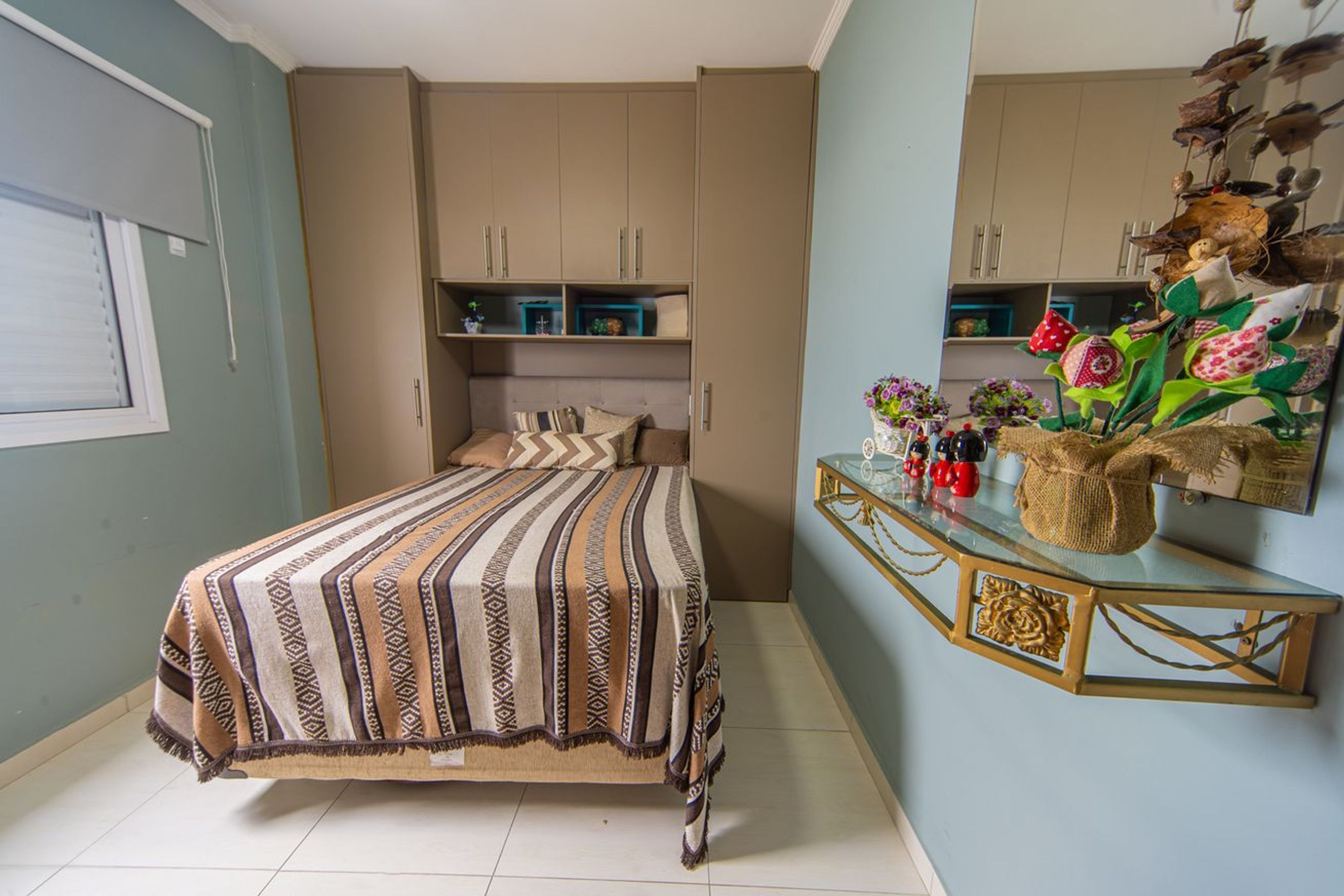Un dormitorio con cama, cómoda y estante en la pared con objetos decorativos.