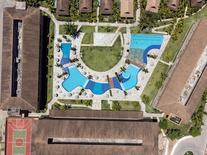 An aerial view of a resort with multiple swimming pools, a tennis court, and surrounding greenery. - Exclusive Oceanfront Bungalow with Included Service Eco Resort Carneiros (Praia dos Carneiros)