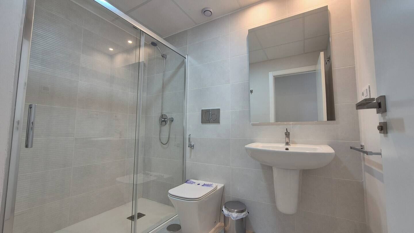 Un baño moderno con cabina de ducha de vidrio, un lavabo blanco y un espejo sobre el lavabo.