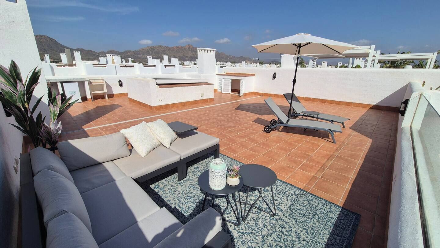En tagterrasse med sofa, loungesæder, et bord og en parasol.