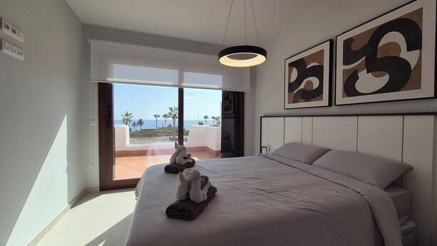 Une chambre d’hôtel avec un lit, une vue sur les palmiers et la mer, et une œuvre d’art abstrait accrochée au mur.