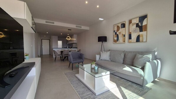 A modern living room with a sofa, coffee table, and a TV. There is a kitchen area in the background.