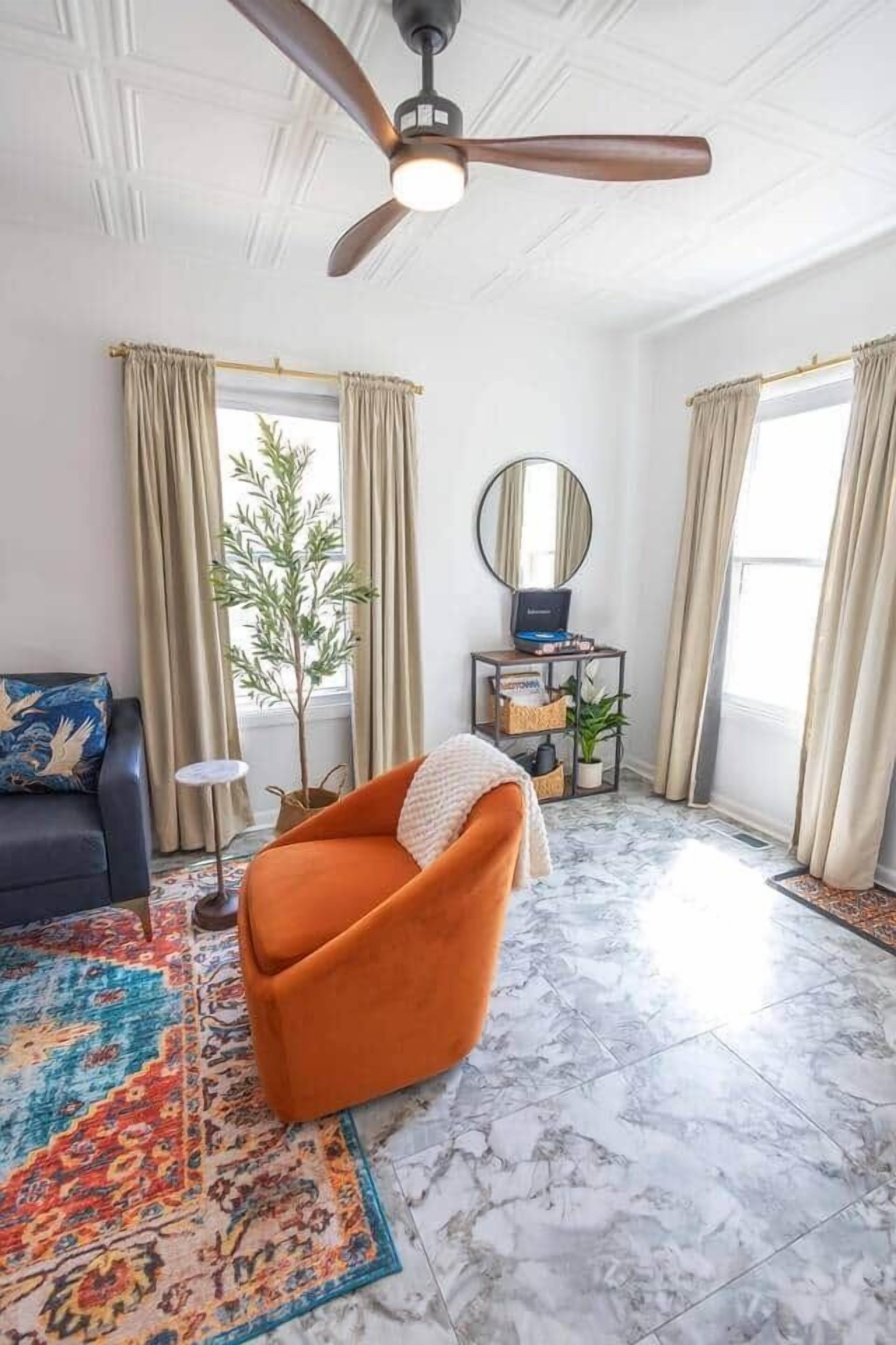 A living room with a ceiling fan, a sofa, a coffee table, a small side table, a potted plant, and a window with curtains.