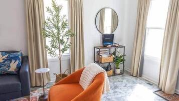 A living room with a ceiling fan, a sofa, a coffee table, a small side table, a potted plant, and a window with curtains.