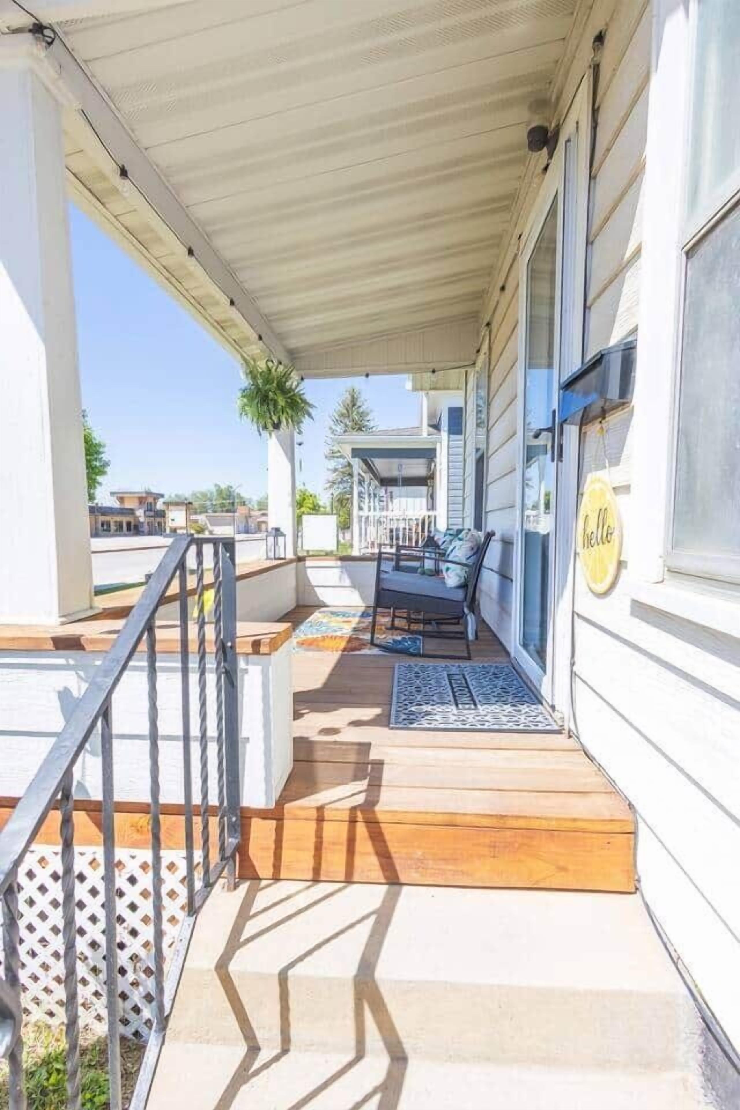 A covered porch with a wooden deck, a metal railing, a bench, and a 'hello' sign on the wall.