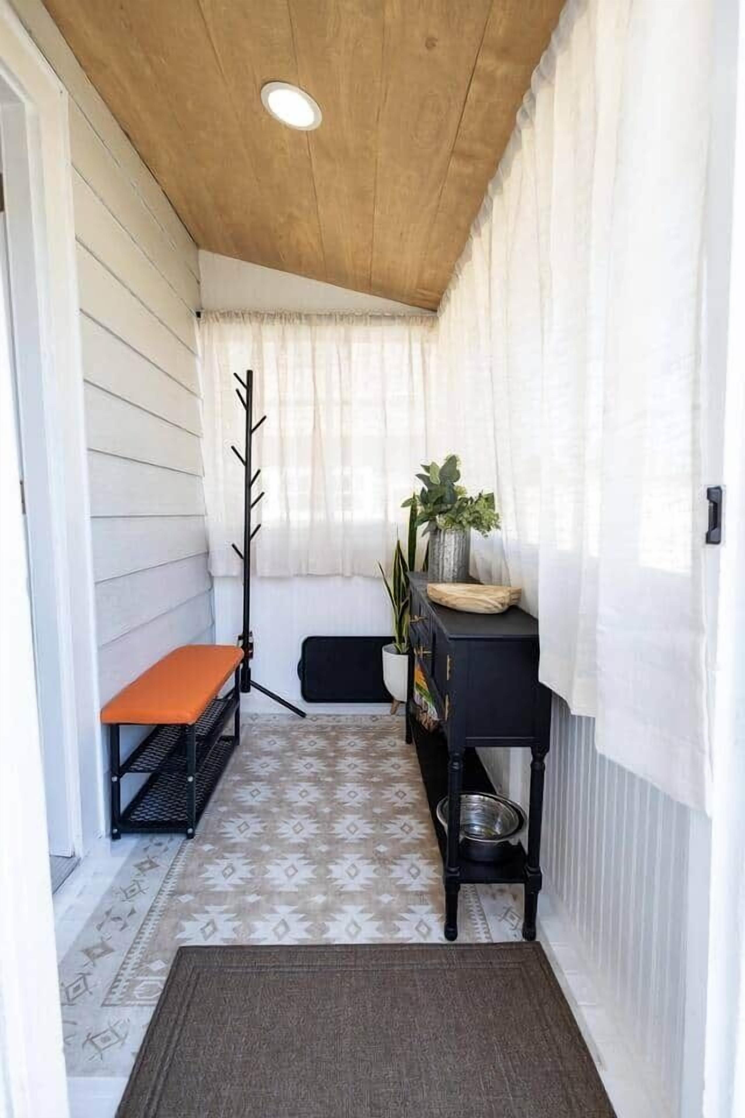 En smal gang med en bænk, knagerække, et lille bord med en plante og et tæppe.
