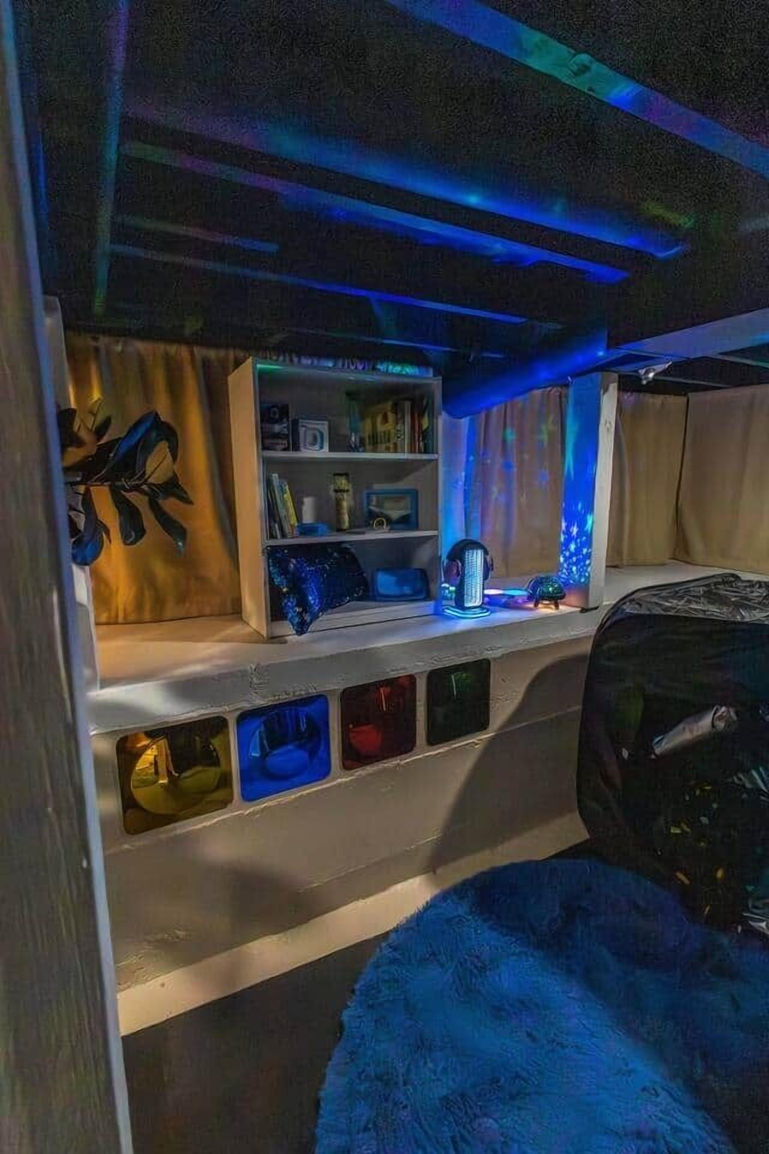A room with a bunk bed, a shelf with various items, and a blue light strip on the ceiling.