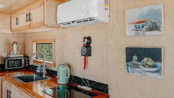A kitchen with wooden cabinets, a microwave, a kettle, a sink, and a wall-mounted air conditioner.