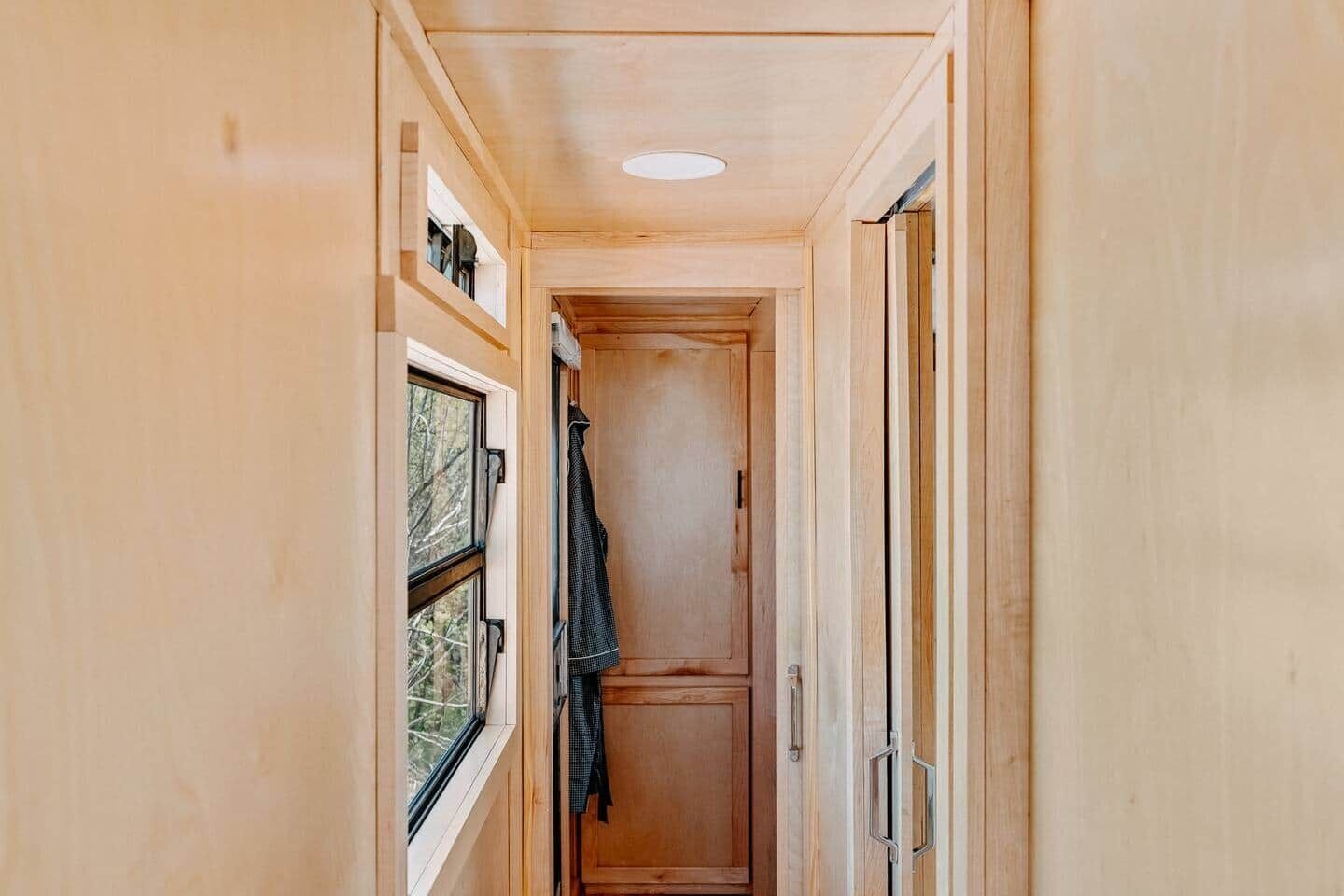 A narrow hallway with wooden walls, a window on the left, and a door on the right.