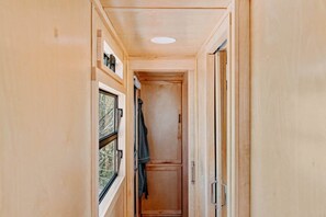 A narrow hallway with wooden walls, a window on the left, and a door on the right.