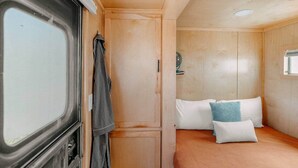Una camera compatta con un letto, cuscini, un appendiabiti e una piccola finestra.