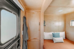 A compact bedroom with a bed, pillows, a hanging garment, and a small window. - The 56 · A Spartan Royal Manor · Dogs Welcome (Sheridan)