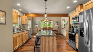 A kitchen with wooden cabinets, a central island, stainless steel appliances, and a dining area with chairs.