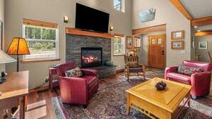 A living room with a fireplace, red leather sofas, a television, and a large window.