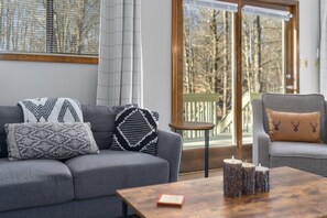 A modern living room with a grey sofa, patterned cushions, a small round table, and a coffee table with candles. - Superb 4-bedroom house with wrap around deck in charming Pocono Lake (Pocono Lake)