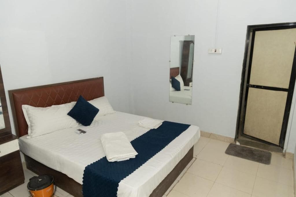 Une chambre d’hôtel avec un lit, un miroir, une porte et une poubelle.
