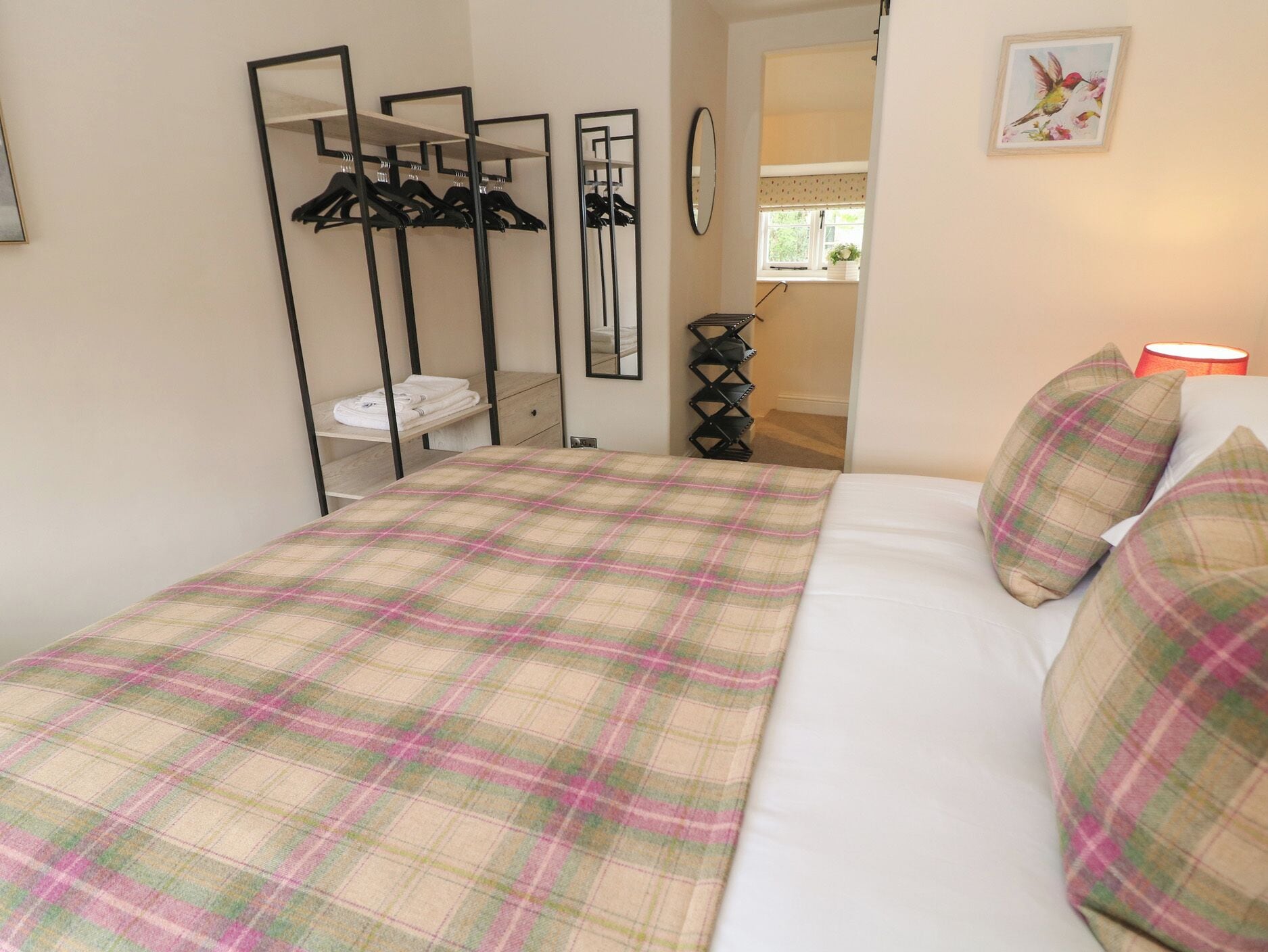 A bedroom with a bed, a wardrobe, a mirror, a hanging shoe rack, and a window with a view.
