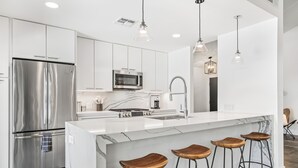 Une cuisine moderne dotée d’appareils électroménagers en acier inoxydable, de meubles blancs, d’un îlot en marbre et de tabourets de bar en bois.
