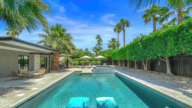 Une piscine avec des chaises longues, des palmiers et un espace patio.