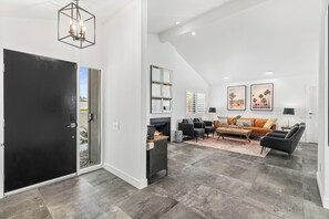 Ein geräumiges Wohnzimmer mit Kamin, einer schwarzen Tür und einer Decke mit eingelassenen Leuchten.