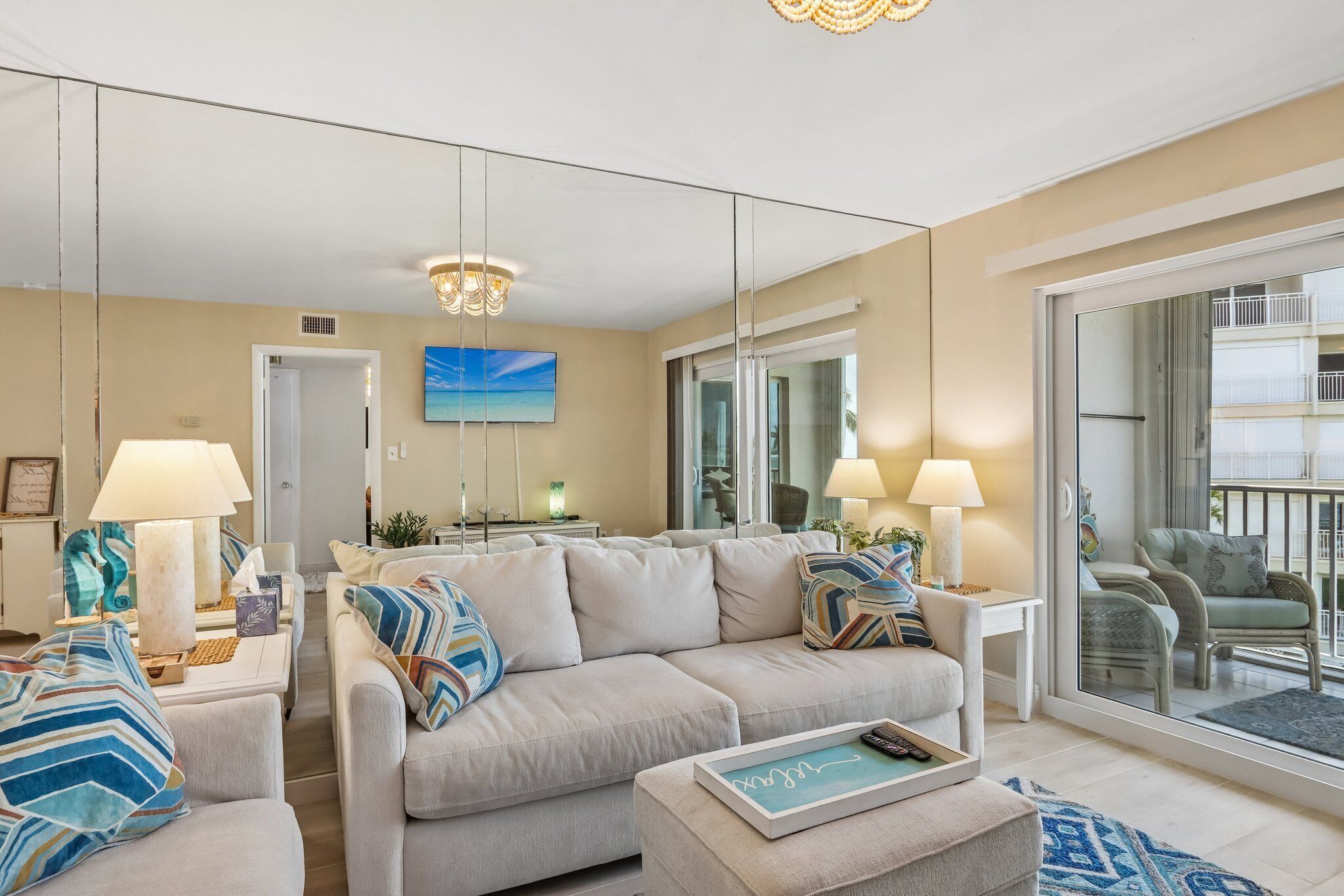 A modern living room with a sofa, two side tables, and a large mirror reflecting the balcony.