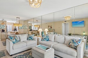 A spacious living room with a large mirror, two sofas, a coffee table, and a television. - Wake up to the sound of waves and breathtaking sunsets over the Gulf! (Fort Myers Beach)