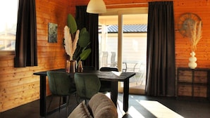 Un intérieur en bois comprenant une table à manger, des chaises, un luminaire suspendu et une porte-fenêtre coulissante donnant sur l’extérieur.